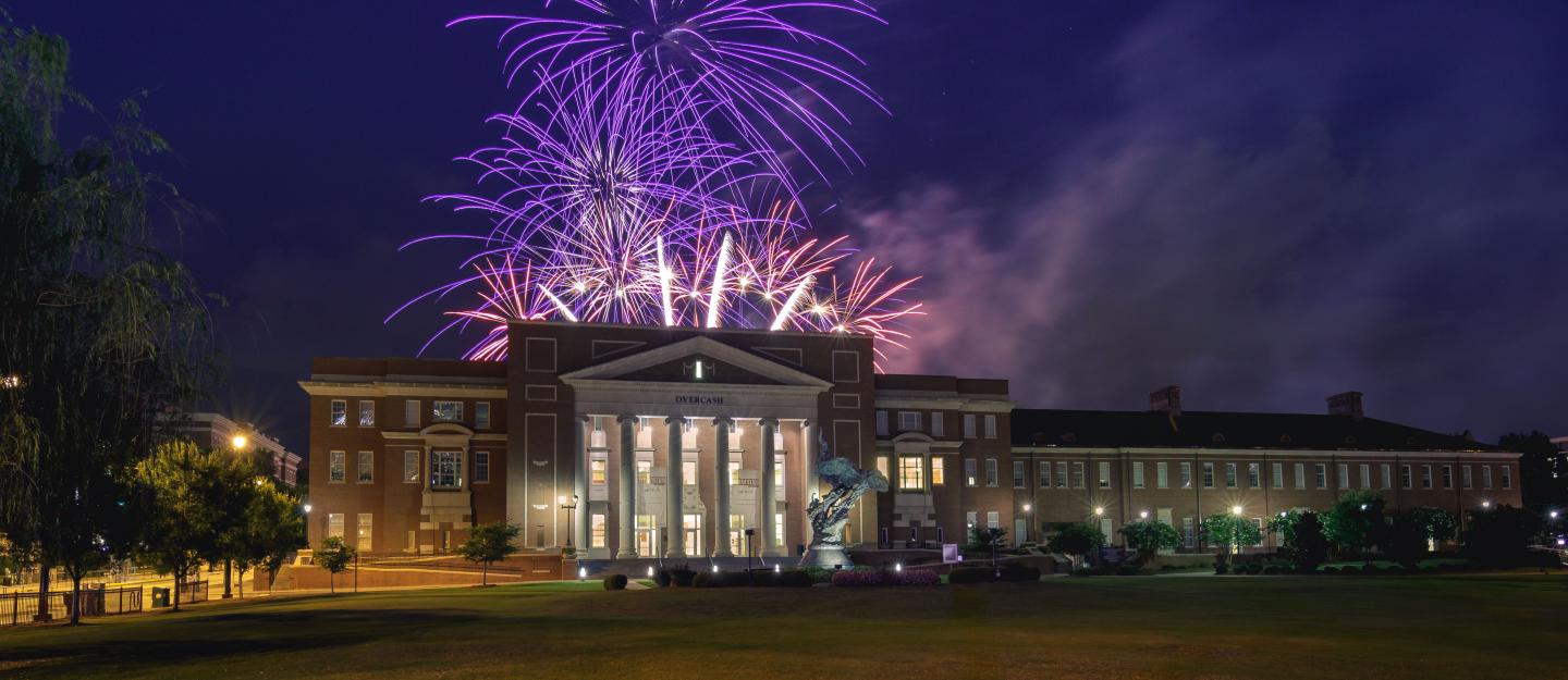 Fireworks bursting above a floodlit campus building at night
