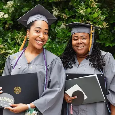 Two graduates in caps and gowns holding diploma folders