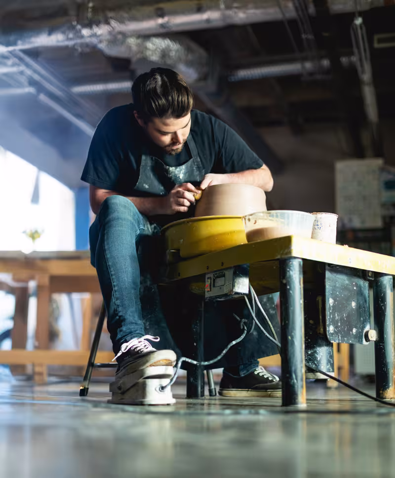 Central Piedmont student concentrating hard while working on clay at pottery wheel in studio.