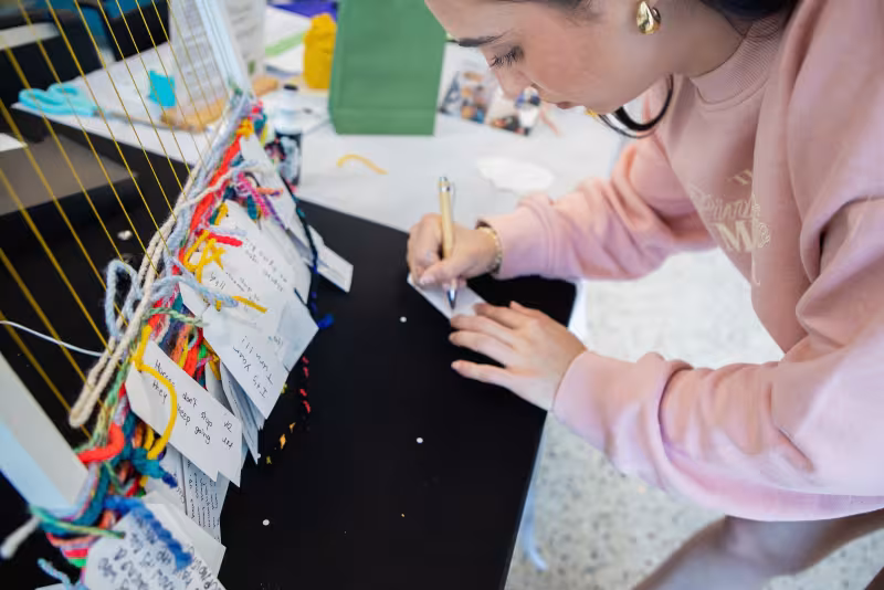 Central Piedmont student bending down to write a message to hang on decorative encouragement art project.