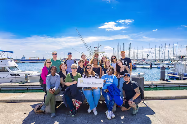 A group of Central Piedmont students on a study abroad trip posing together in front of a harbor.