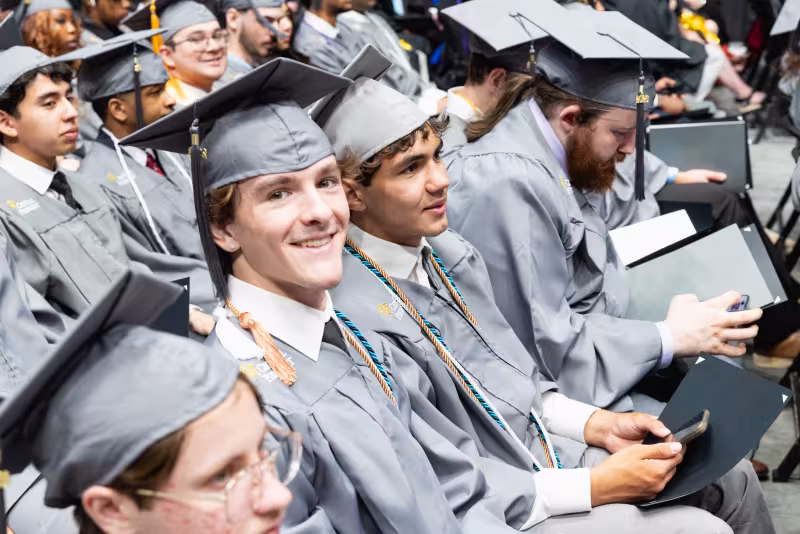 Multiple seated graduates wearing caps and gowns during ceremony