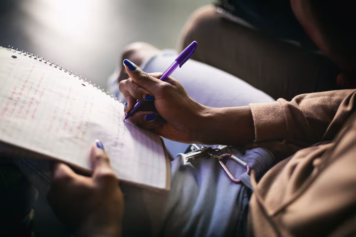 Close-up of a student's hands writing notes in a spiral notebook with a purple pen