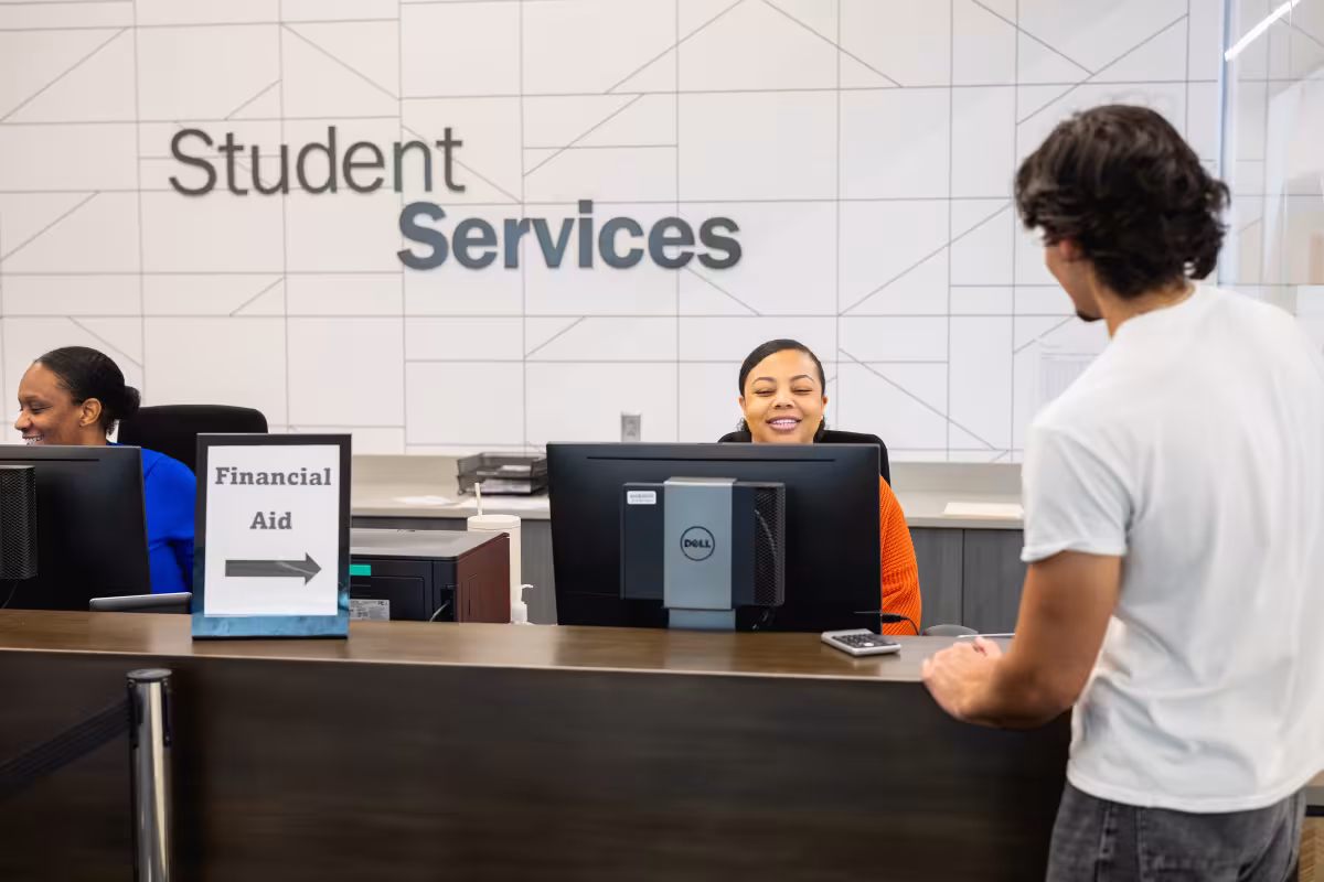 Student at financial aid desk within the student services office talking with a staff member who is sitting behind the desk