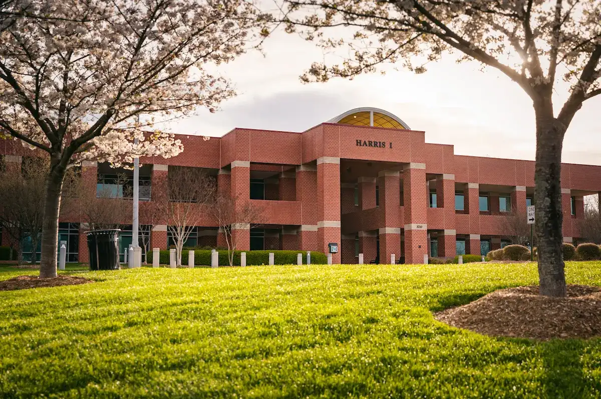 Exterior of brick Harris Building on Central Piedmont’s campus with trees and grass on grounds in foreground.