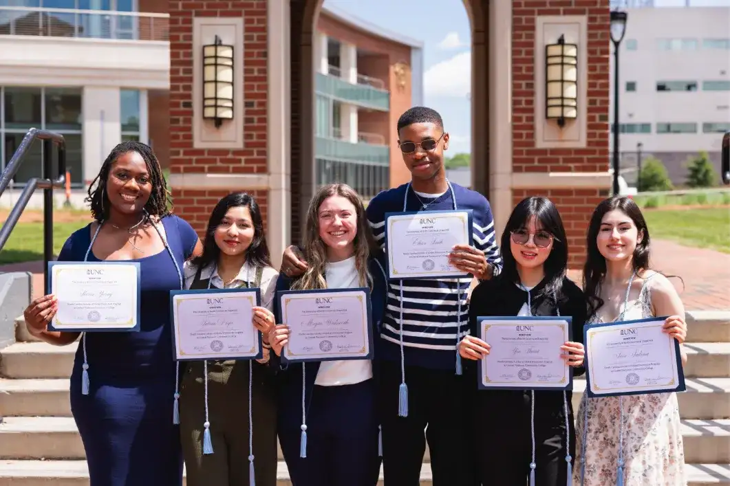 Six smiling Central Piedmont students wearing honors cords and displaying NC Scholars of Global Distinction awards.
