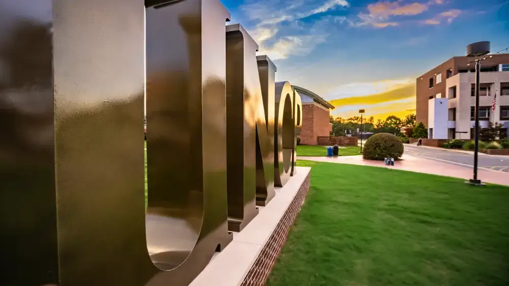 Metal campus lettering at University of North Carolina at Pembroke lit by sunset