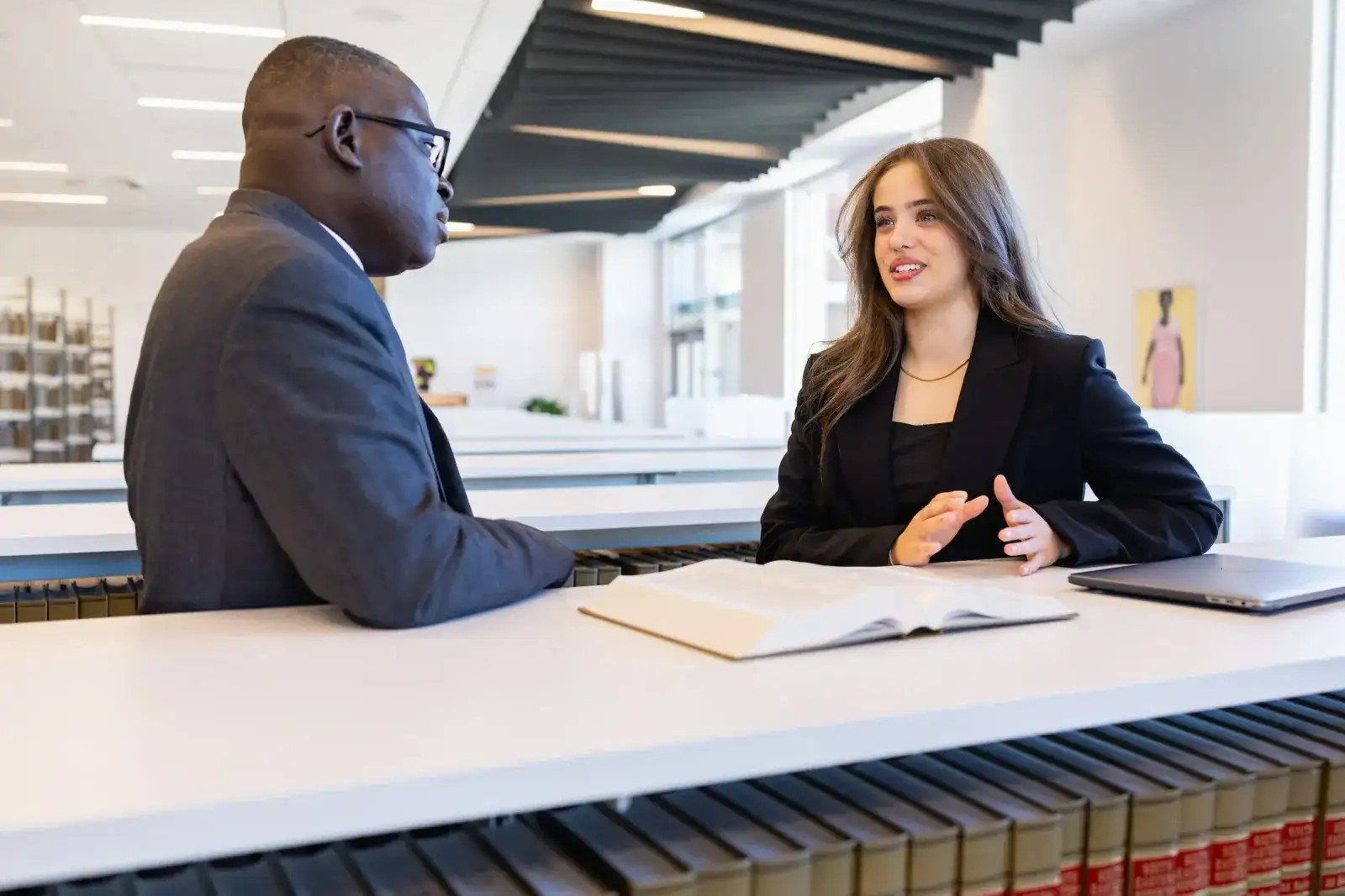 Two business students in professional dress talking across a desk