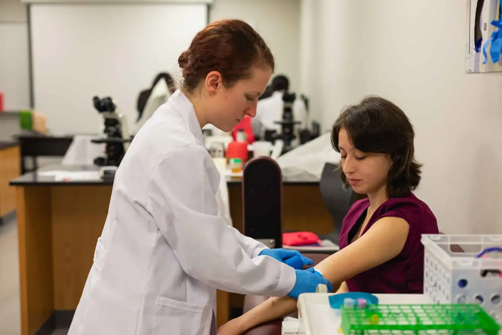 Medical Assisting student in a lab coat drawing a blood sample from a patient