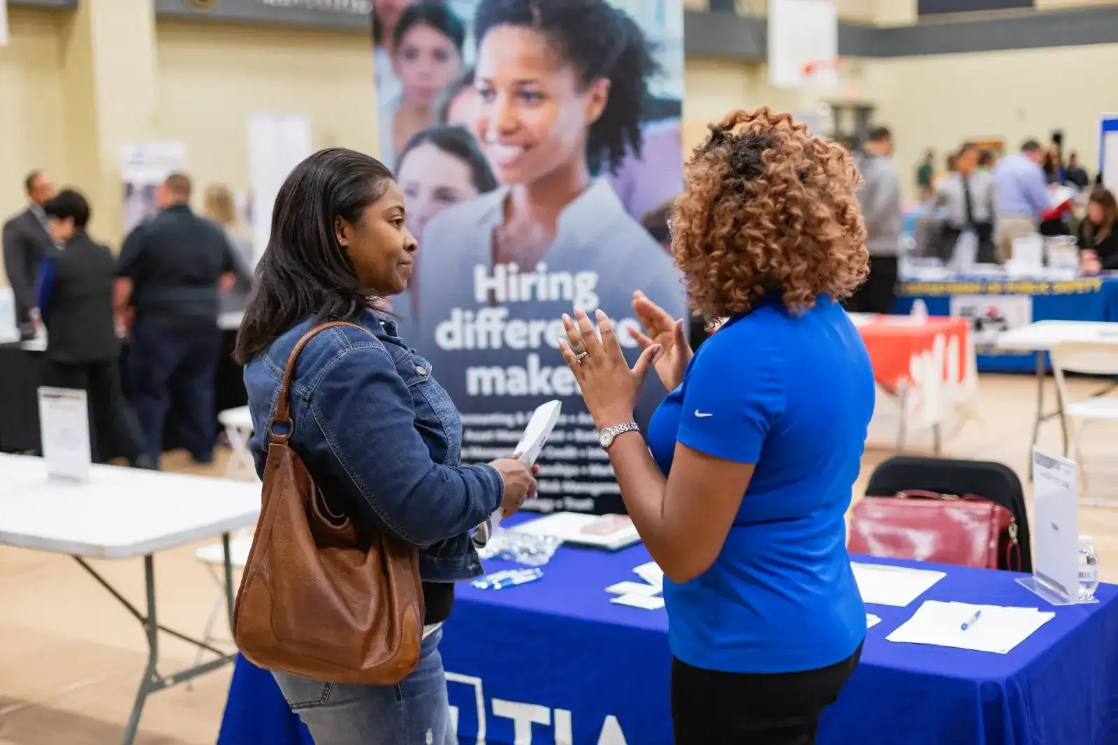 Two people talking at a careers fair beside a hiring banner