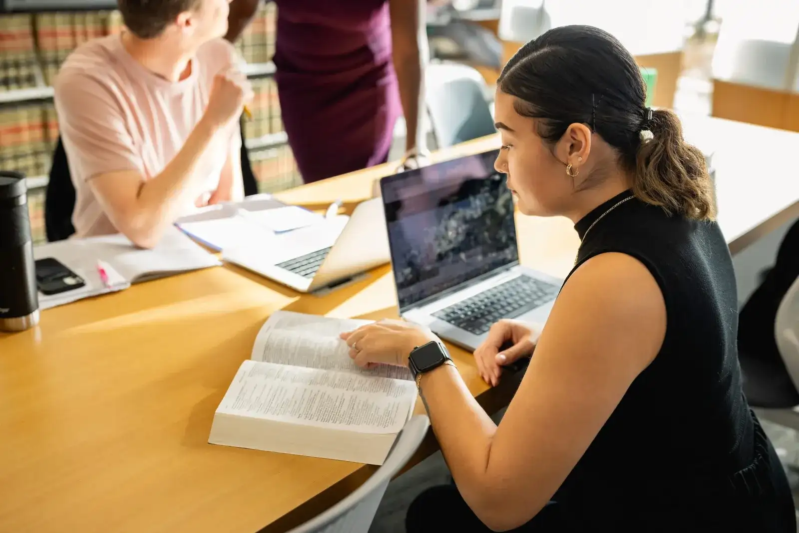 Student researching on a laptop with an open book in the library