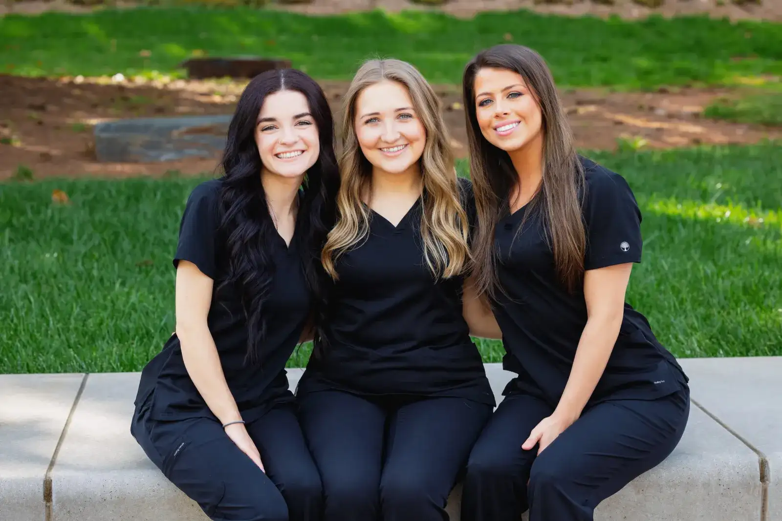 Three students in scrubs sitting together outside on campus