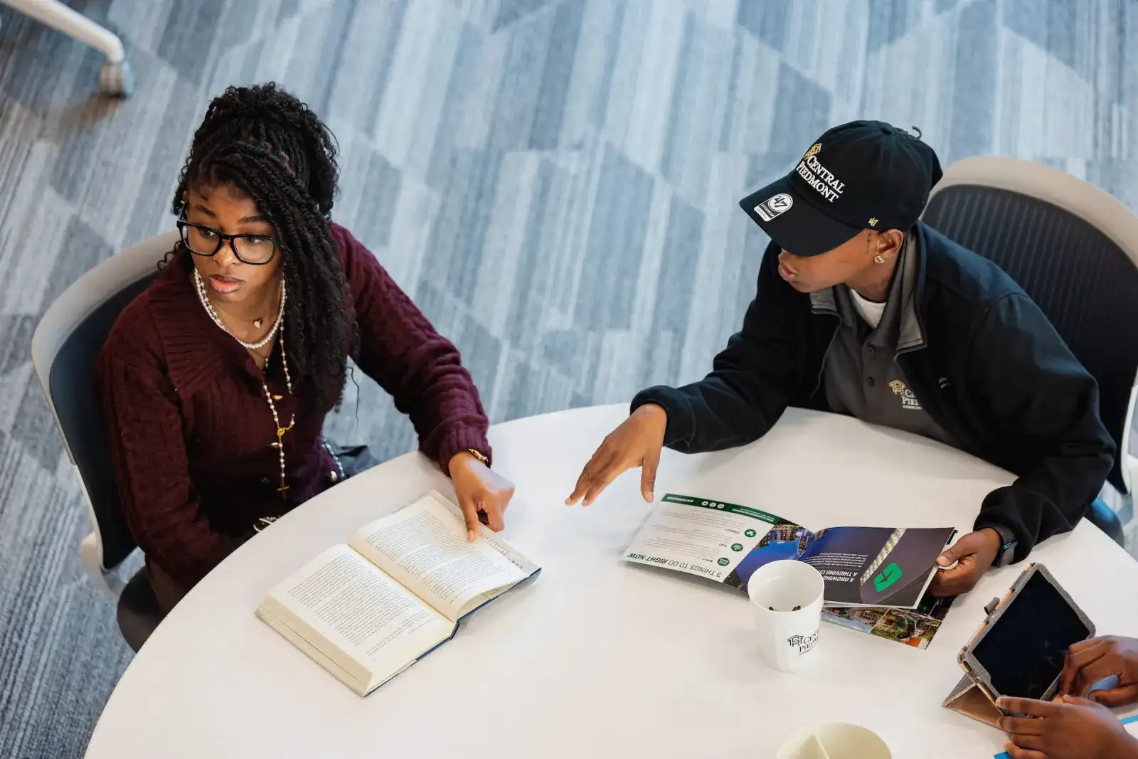 Two students studying with textbooks and a laptop at a table