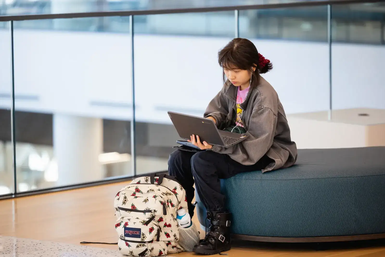 Student using a tablet while sitting on a bench in a campus atrium