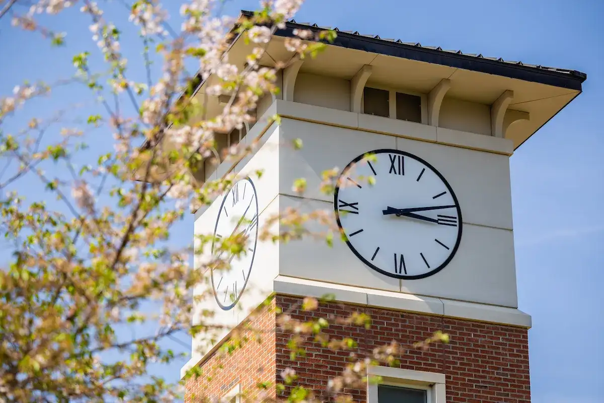 Large clock at top of Central Piedmont campus building tower with tree branches in foreground.