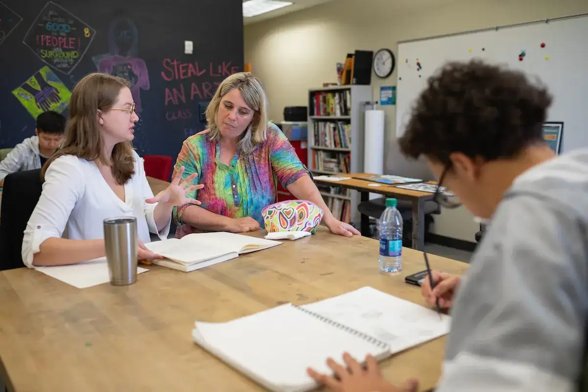 Students gathered at a table with open notebooks and a tutor.