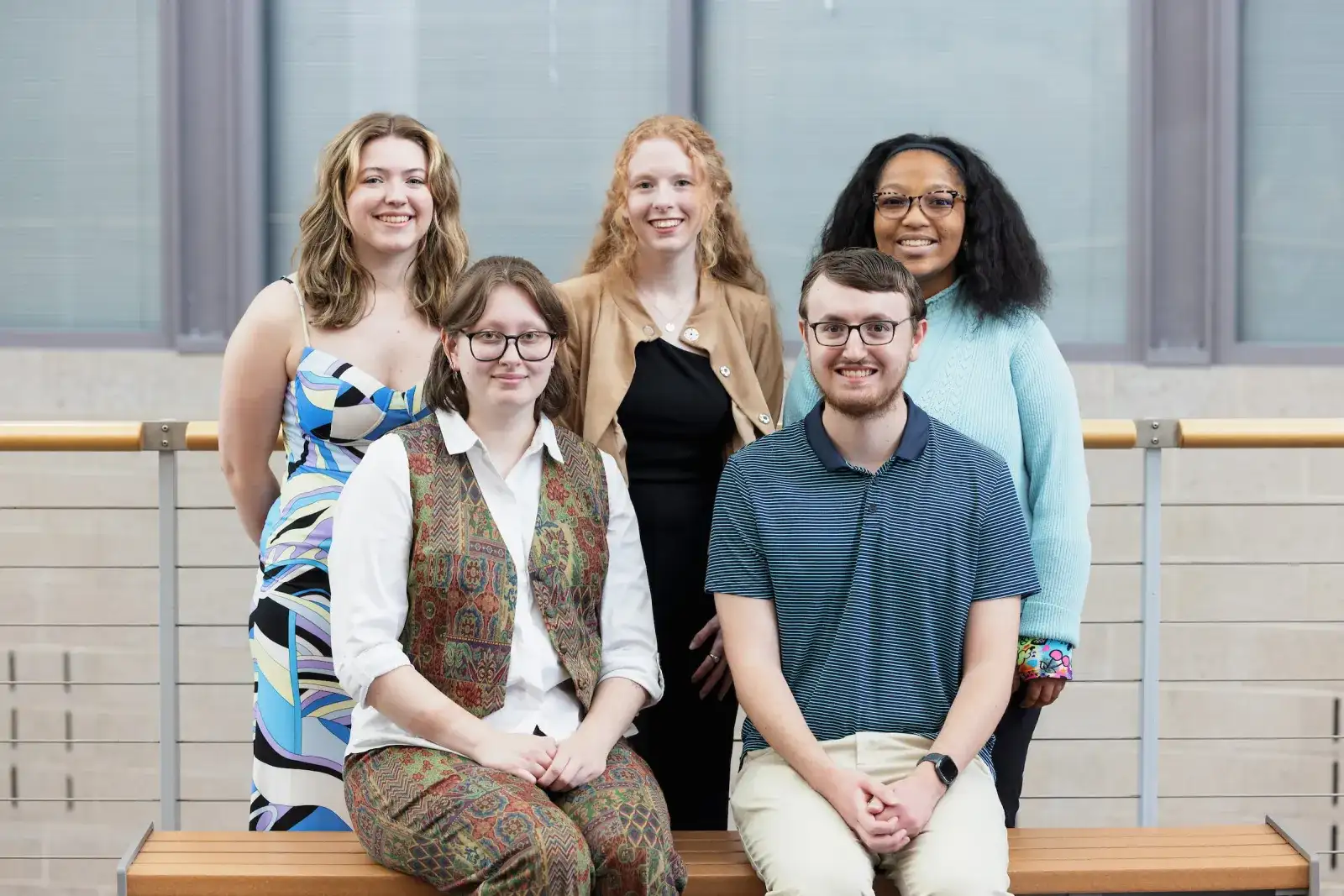 Five students posing together on a bench outside a campus building