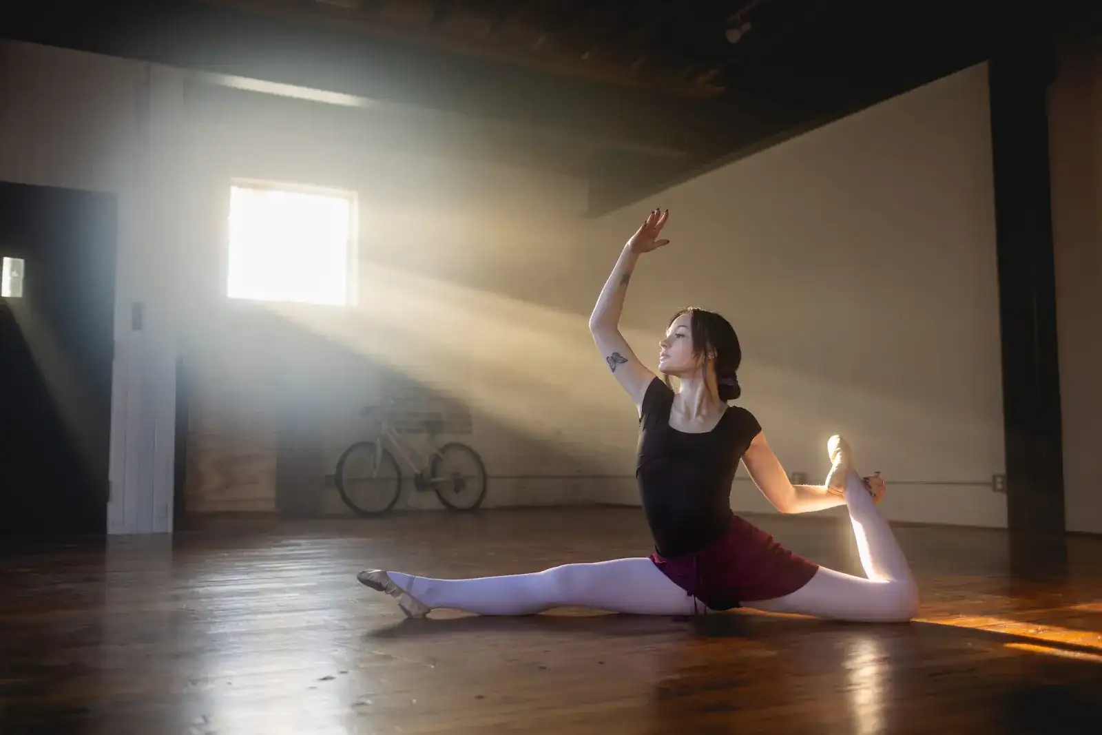 Dancer stretching into a split on a sunlit studio floor