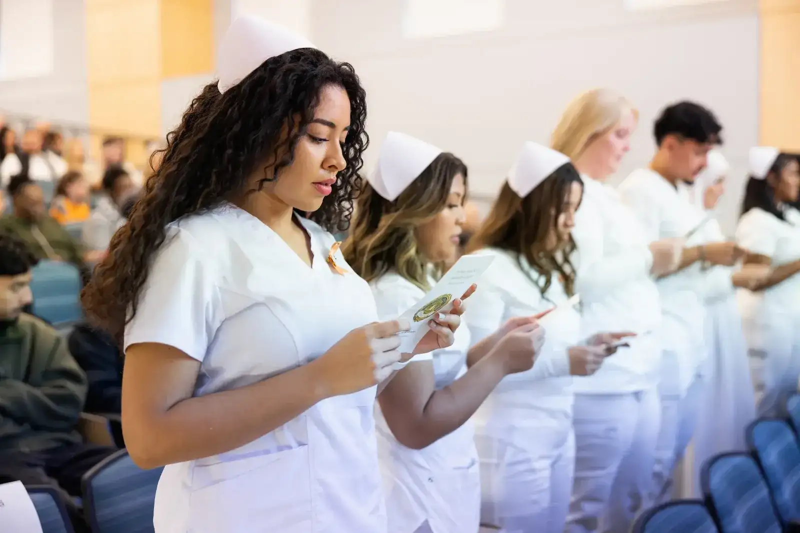 Nursing students in white uniforms and caps lined up at a ceremony