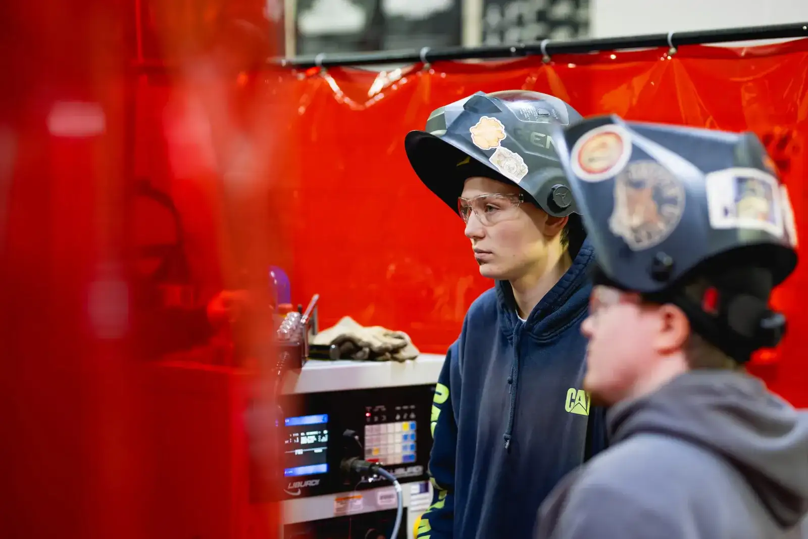 Welding student in a protective helmet talking with an instructor in the welding lab