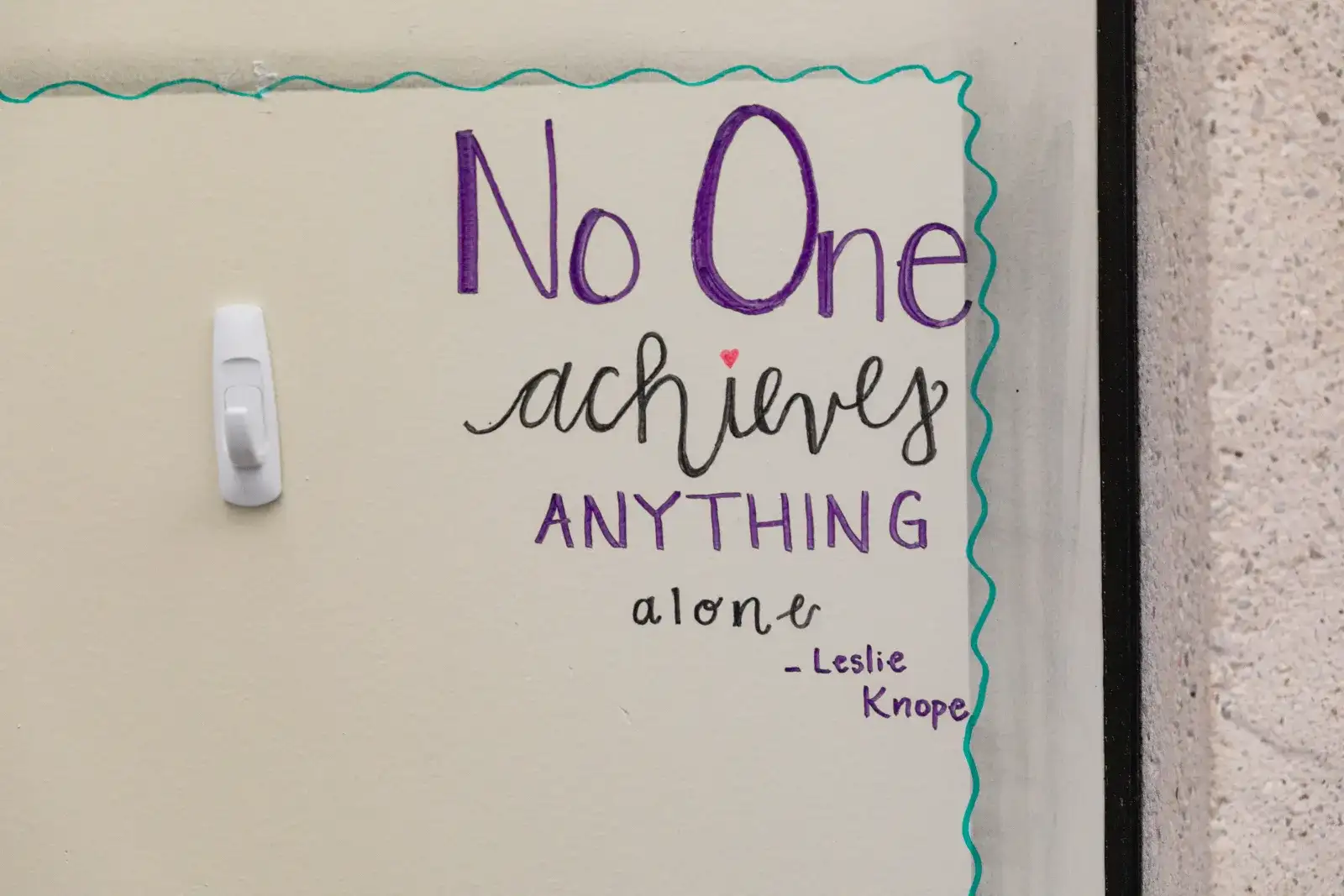 Dry erase board that says "No one achieves anything alone"