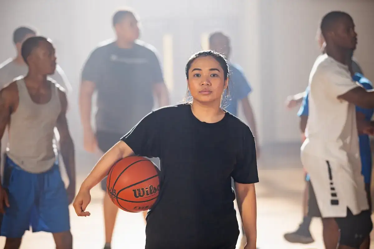 Student standing on a court with other students, holding a basketball
