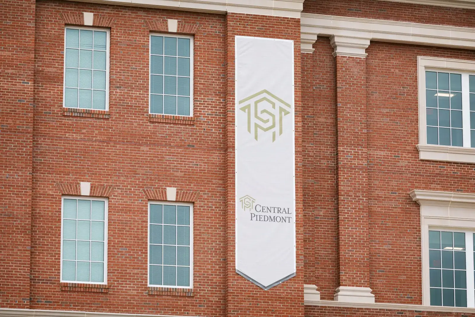 Vertical flag with Central Piedmont logo and name hanging on the outside of a campus building