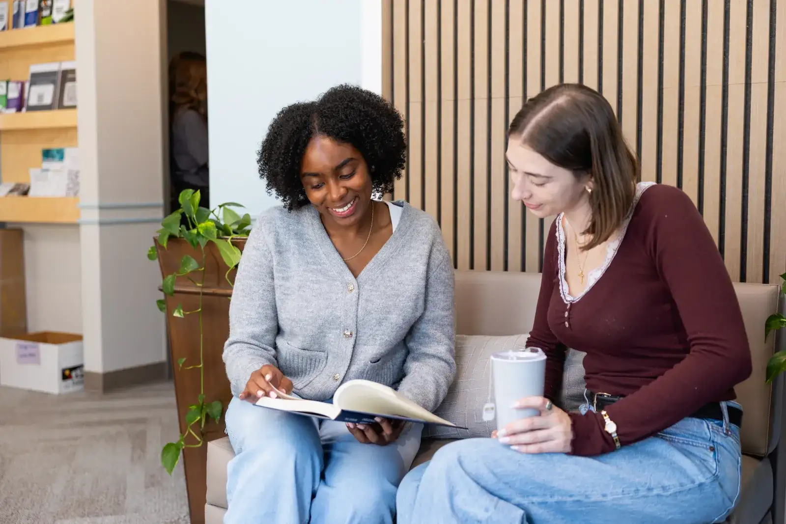 Central Piedmont student and advisor sitting on common area couch, smiling while looking down at textbook.