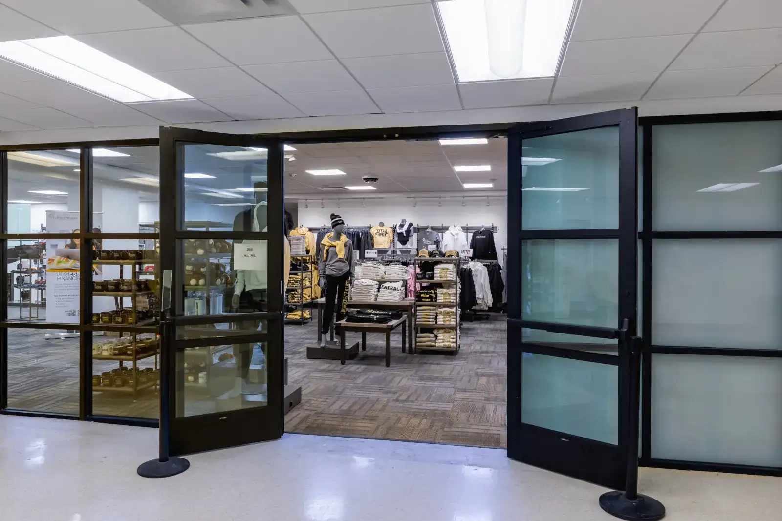 Front of campus store with double glass doors open and selection of clothing and supplies inside