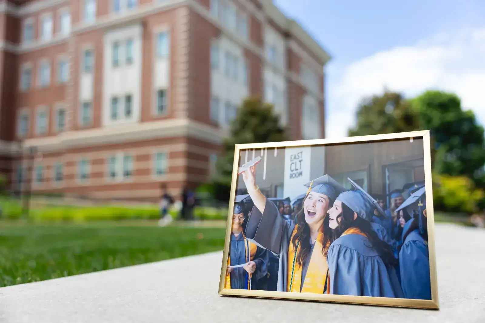Framed photograph of graduates propped on the lawn in front of a campus building