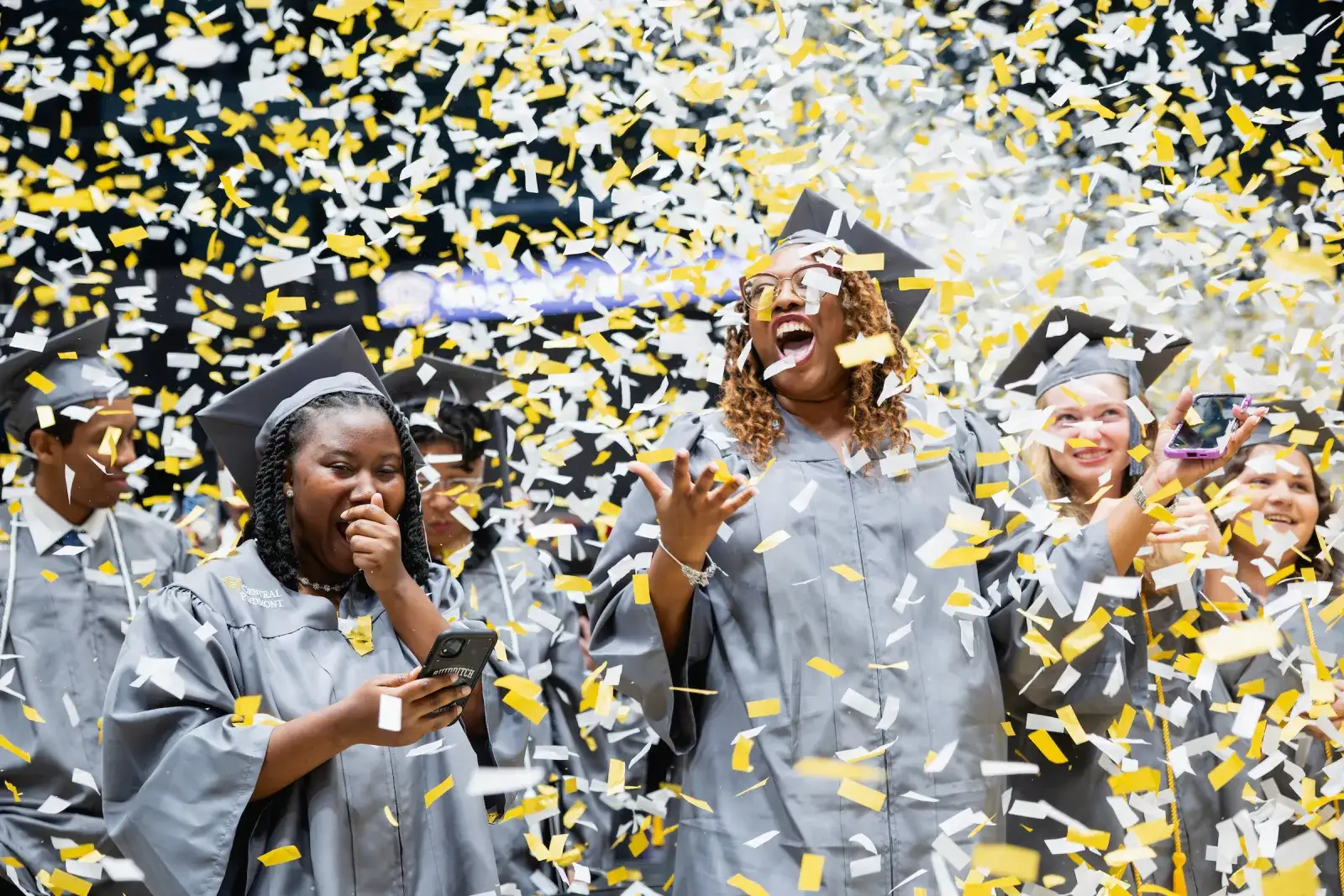 Graduates celebrating as gold and black confetti falls