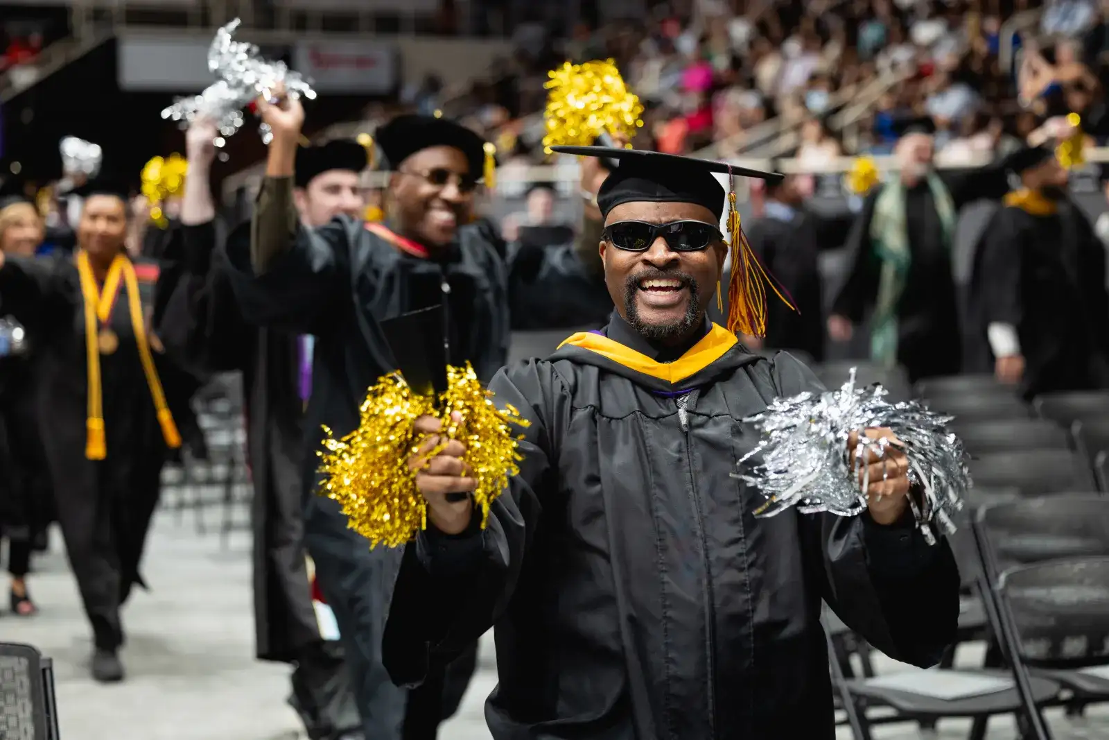 Faculty walking into graduation with pom poms