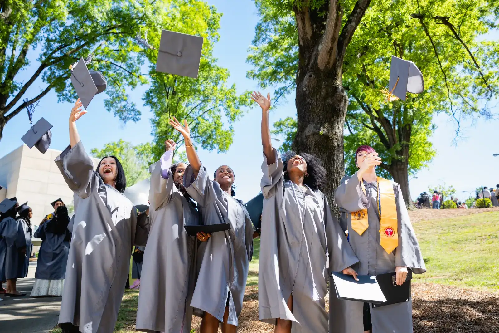 Five recent graduates outside tossing their caps in the air in celebration of their commencement