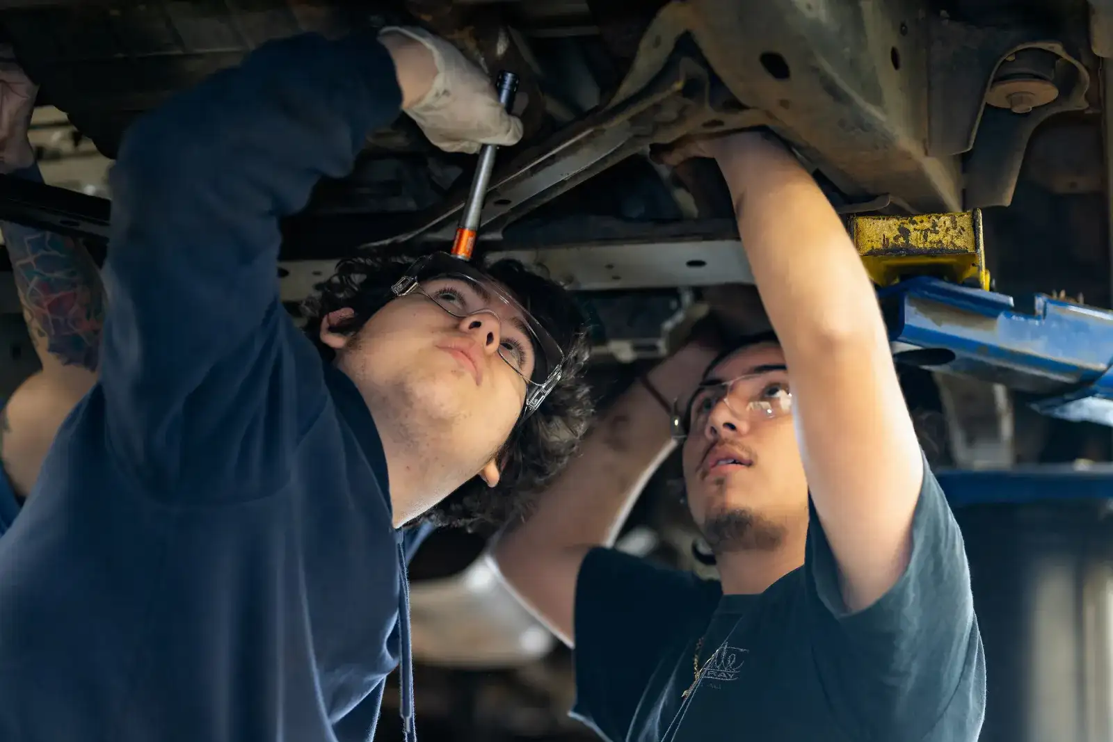 Two automotive students working beneath a raised car