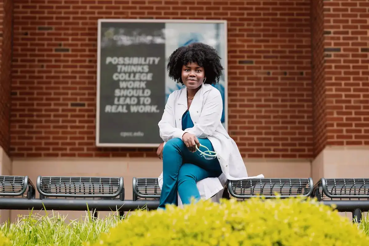 Medical Laboratory Technology student sitting outside in scrubs and a lab coat