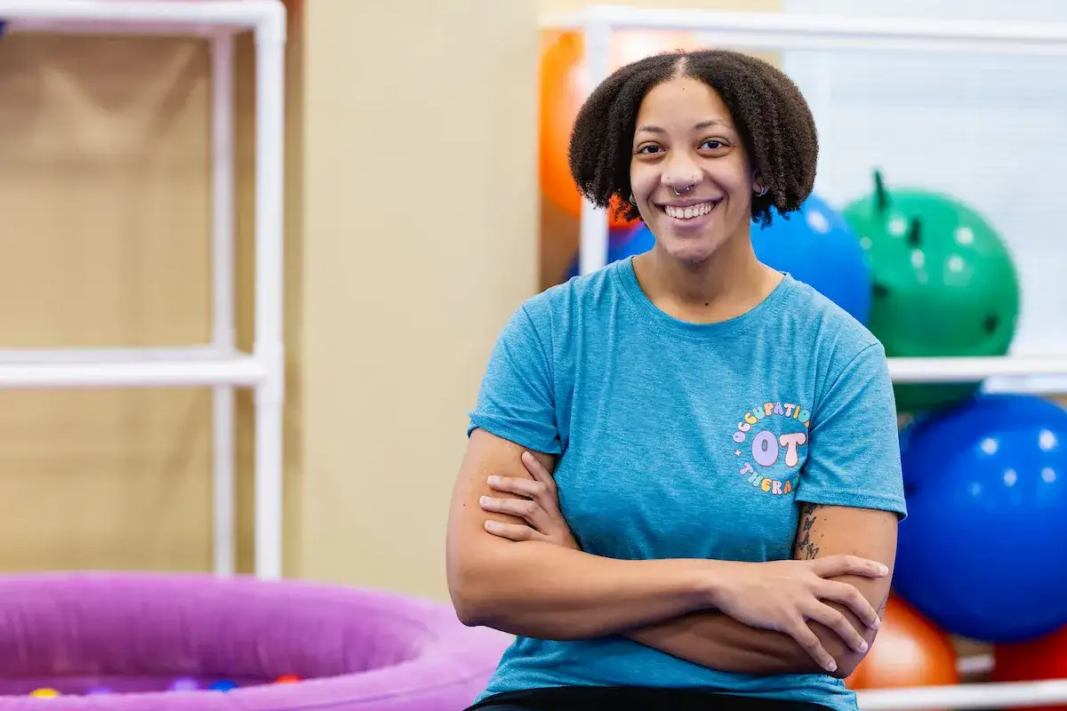 Occupational Therapy Assistant program student standing with arms crossed and smiling in an occupational therapy space