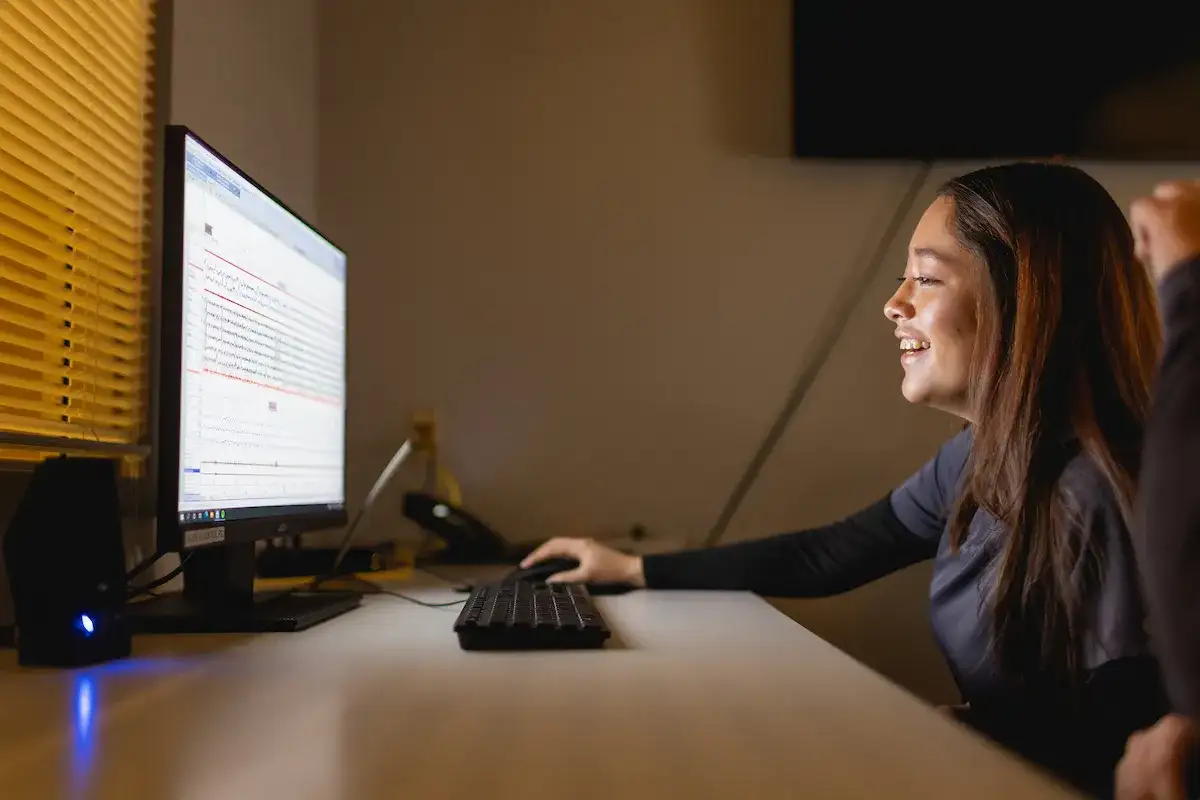 Student smiling and wearing scrubs while seated at a computer