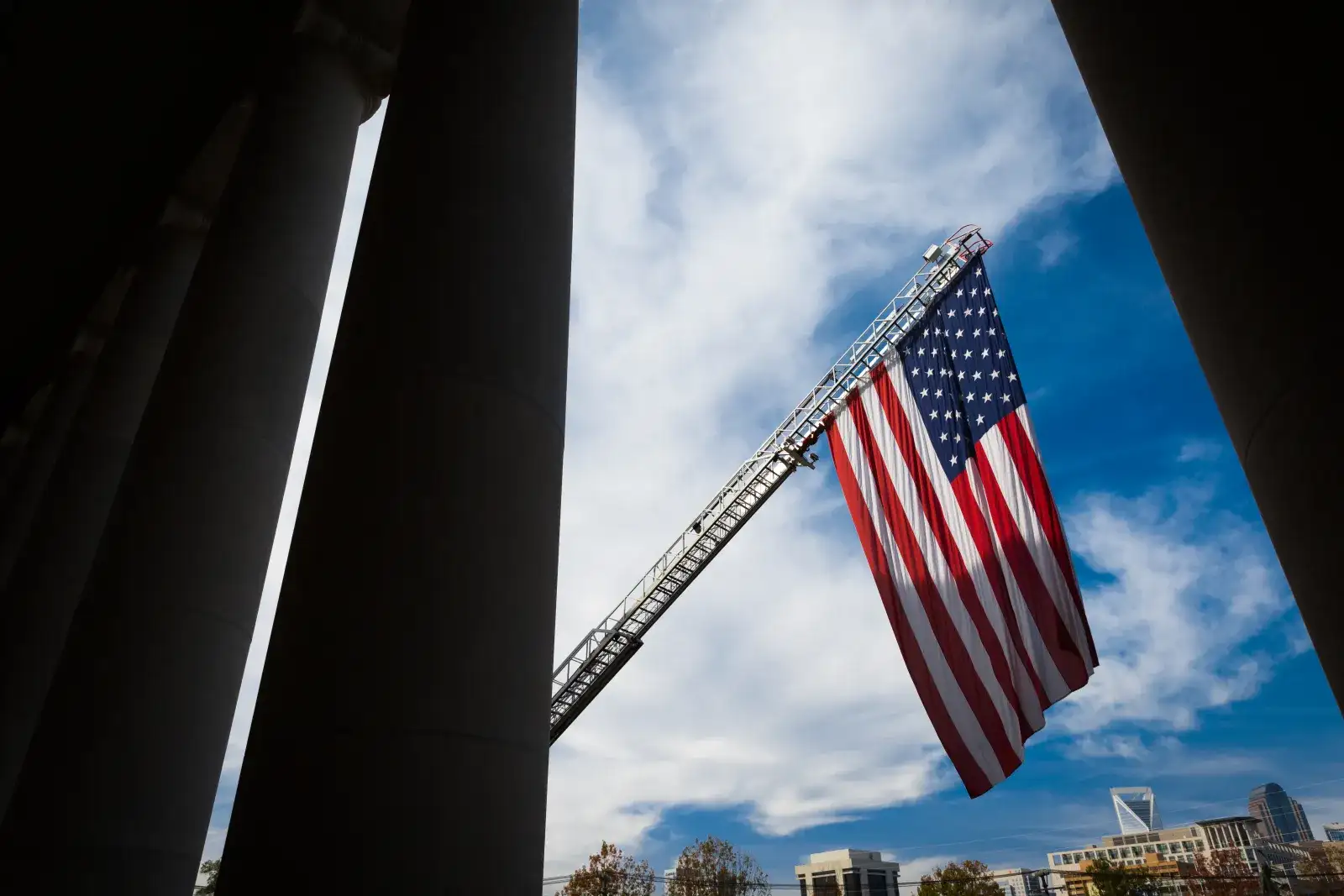 American flag attached to crane with blue sky and clouds in the background