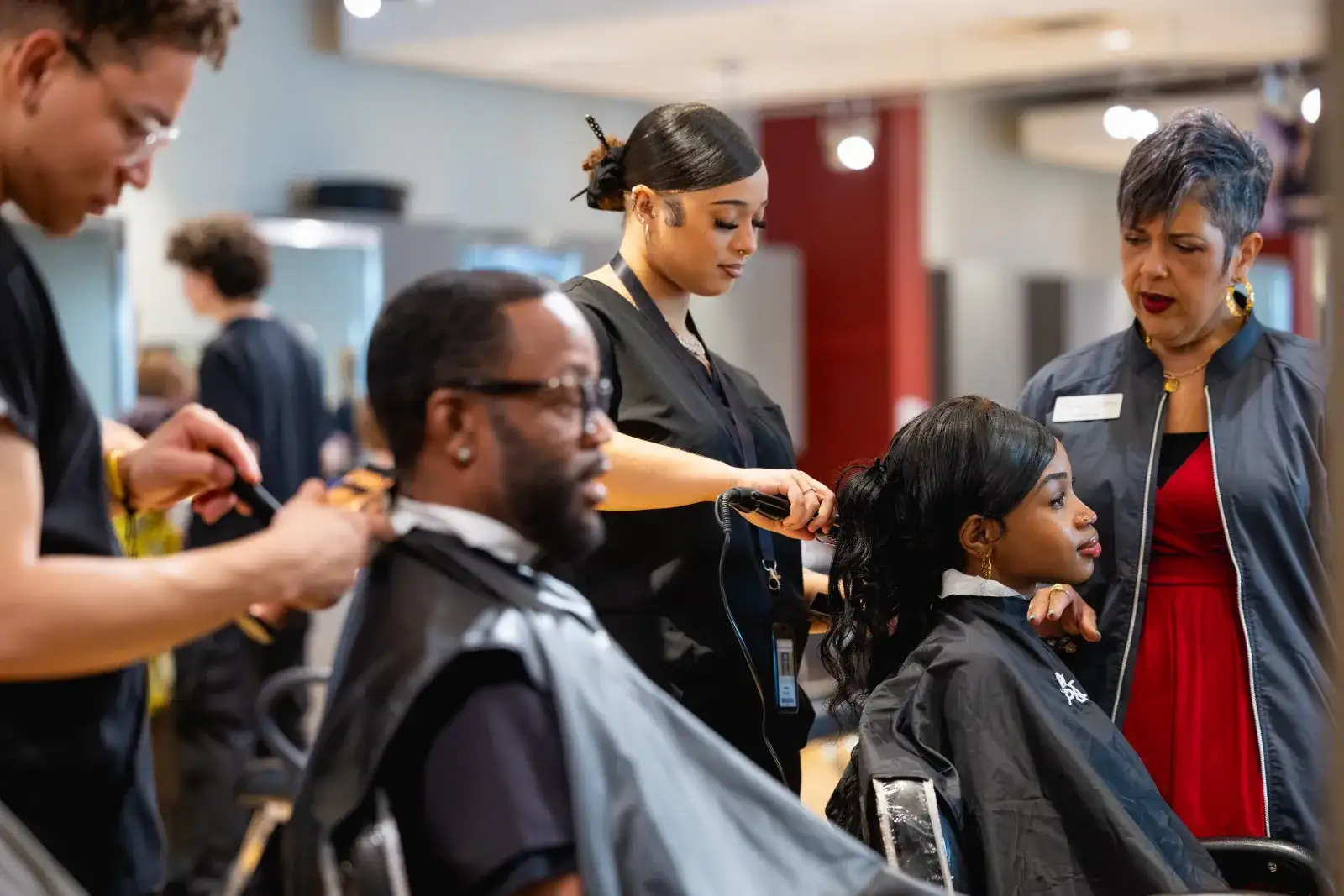 Two students cutting and styling hair on two clients with the oversight of an instructor