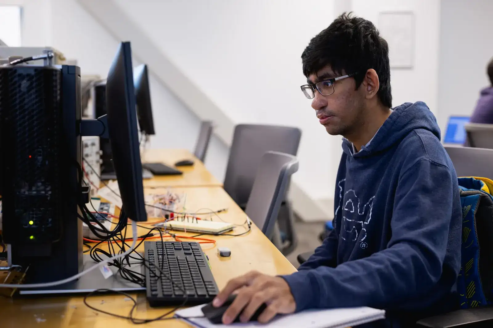 Student at a table with computer tower, keyboard, mouse and wires looking intently at the screen.