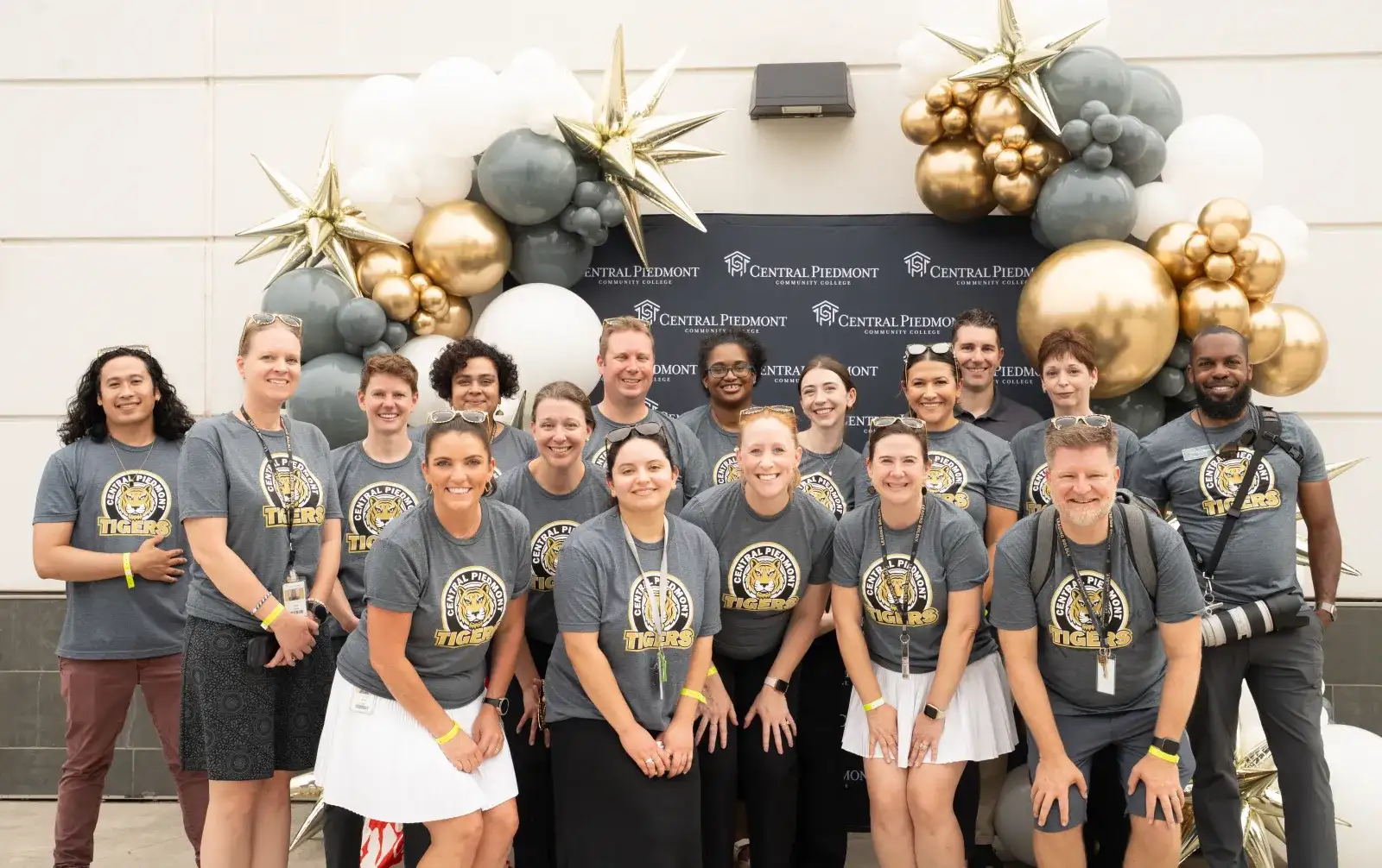 Marketing associates in matching tshirts with the college tiger mascot under a balloon arch 