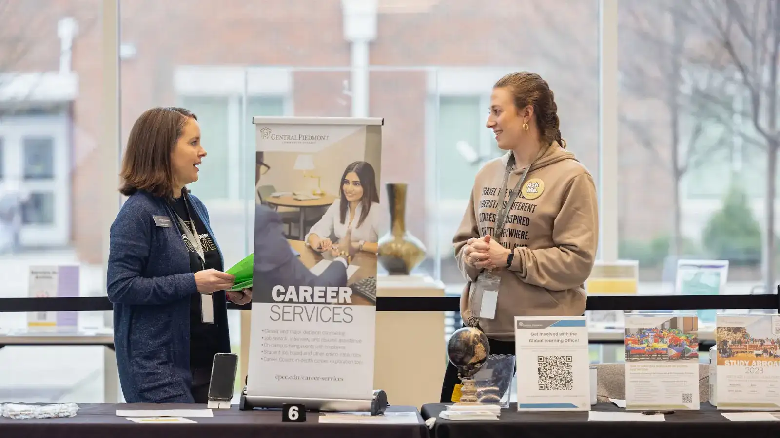 Two Central Piedmont staff members at career services booth holding information and reading materials.