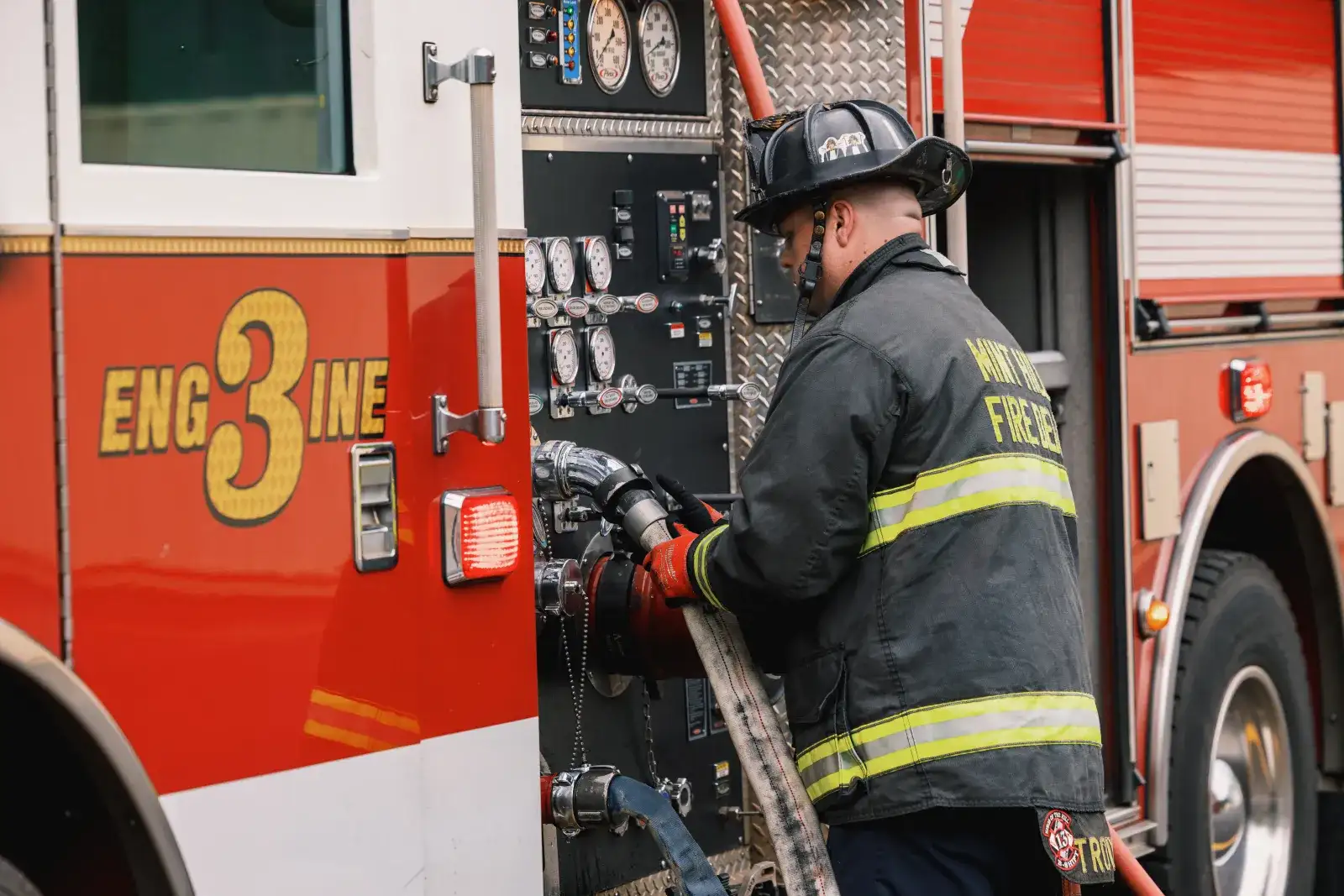 Firefighter in full gear and helmet hooking up a hose to a fire truck