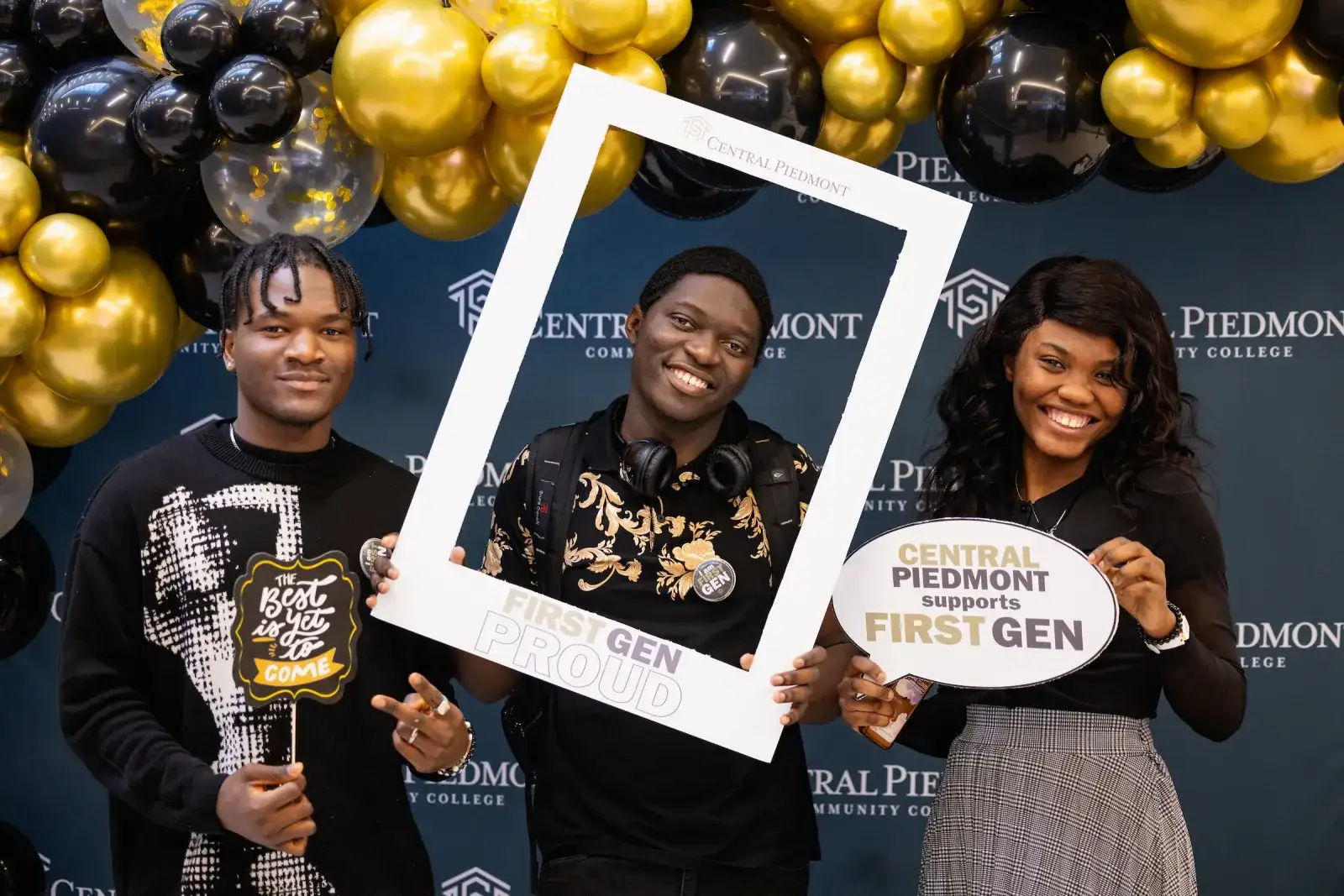 Three first generation Central Piedmont students smiling in front of a balloon arch