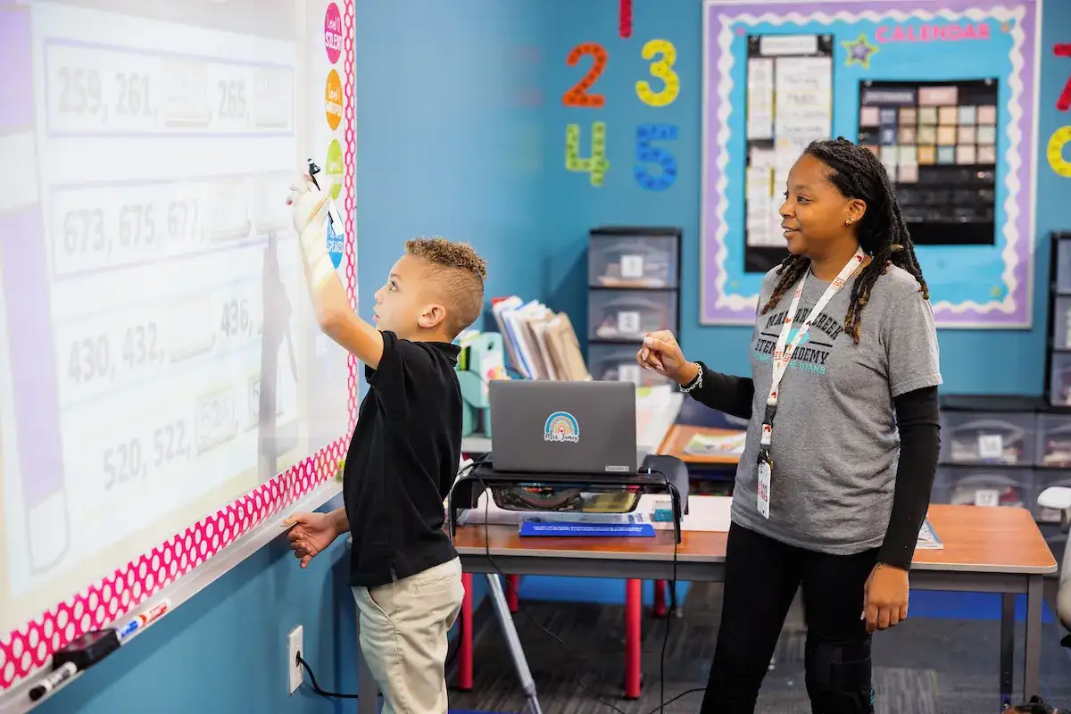 Teacher in training standing at the whiteboard with a young student