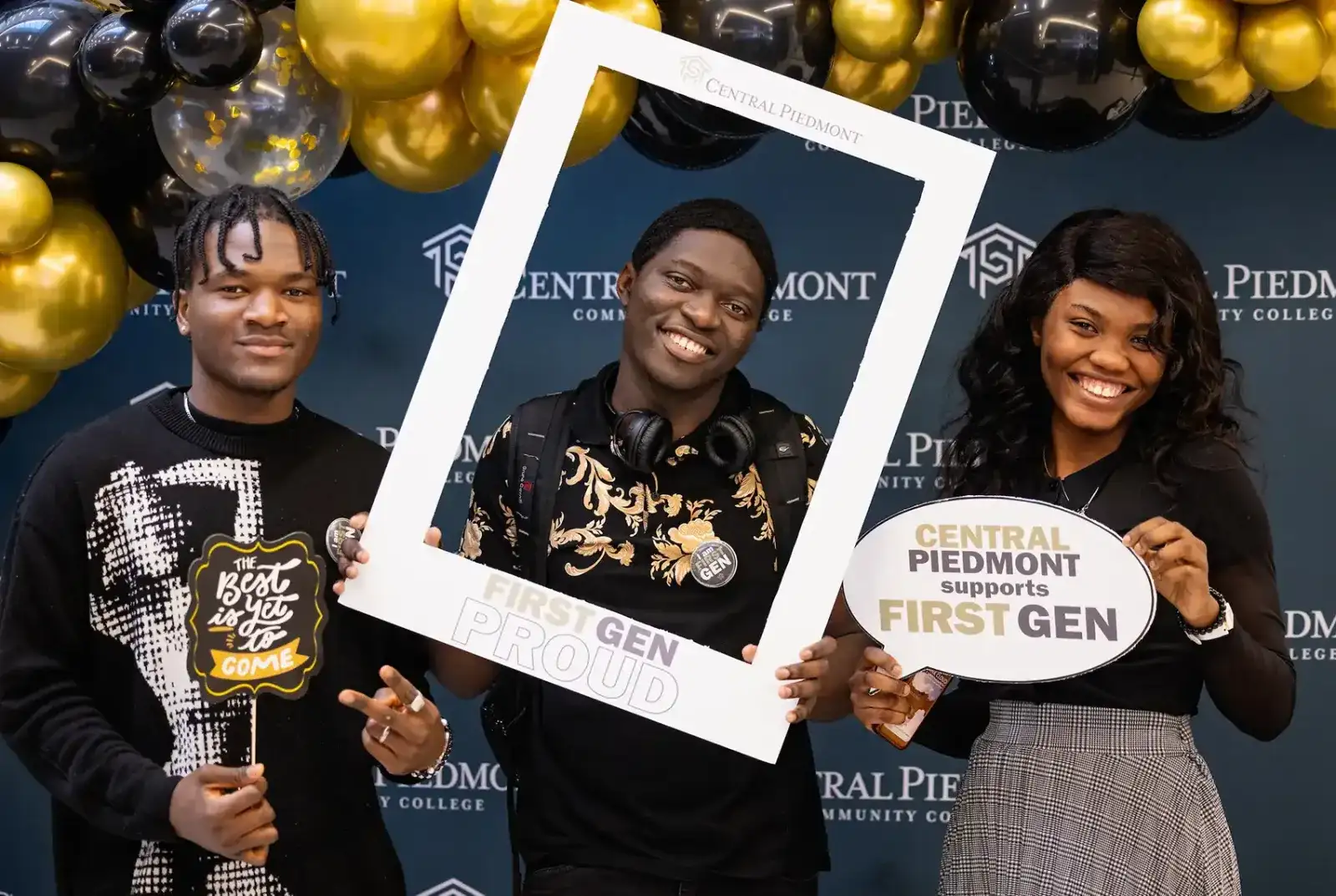 Three first generation Central Piedmont students smiling in front of a balloon arch