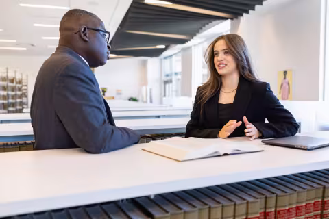 Two business students in professional dress talking across a desk