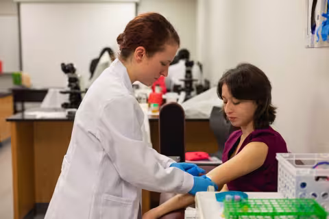Medical Assisting student in a lab coat drawing a blood sample from a patient