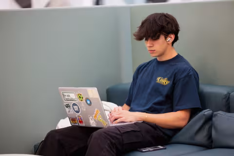 Student working on a sticker-covered laptop on a lounge sofa