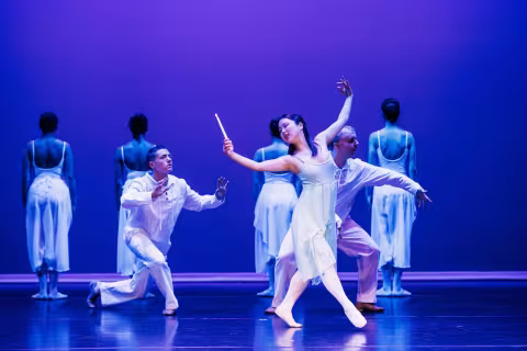 Dancers in white costumes performing on a blue-lit stage